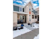 Tan two-story townhome with a covered porch, landscaping, and snow on the ground at 9711 W Indore Dr, Littleton, CO 80128