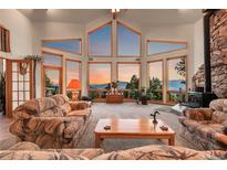 Spacious living room features stunning mountain views from expansive windows and a cozy stone fireplace at 13954 Pine Country Ln, Conifer, CO 80433