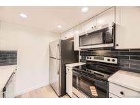 A modern kitchen with stainless steel appliances, sleek black backsplash, and white cabinets at 4691 S Decatur St # 215, Englewood, CO 80110