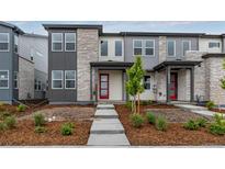 Modern townhome featuring a stone facade, a red front door, and professional landscaping at 20520 E 58Th Ave, Aurora, CO 80019
