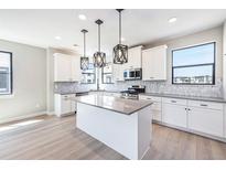 Bright kitchen features an island, stainless steel appliances, modern hanging lights, and gray countertops at 2078 S Holly St # 1, Denver, CO 80222