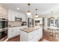 Bright kitchen featuring white cabinetry, stainless steel appliances, a granite island and modern lighting at 3577 S Hillcrest Dr, Denver, CO 80237