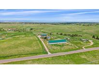 Expansive aerial view of the property featuring green pastures, multiple buildings, and stunning mountain views in the distance at 9255 N Delbert Rd, Parker, CO 80138