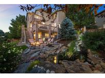 Beautiful backyard featuring a stone patio with a fire pit, waterfall, and lush landscaping at dusk at 10837 Fox Sedge Way, Highlands Ranch, CO 80126