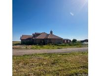 Expansive ranch house with tan exterior, brown roof, and verdant field on a sunny day at 13291 N Harback Rd, Bennett, CO 80102