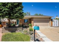 Charming brick home featuring a well-manicured lawn and mature tree with a two-car garage and beautiful landscaping at 8712 W 64Th Way, Arvada, CO 80004