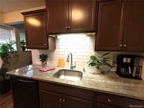 This kitchen features a stainless steel sink, granite counters, tile backsplash, and dark wood cabinets at 10702 E Exposition Ave # 101, Aurora, CO 80012
