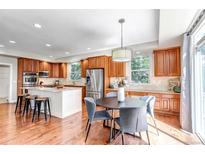 Well-lit kitchen with wood floors, granite countertops, stainless steel appliances, large island, and a round dining table at 10646 Amesbury Way, Highlands Ranch, CO 80126