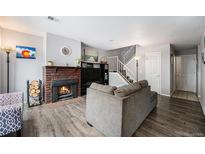 Cozy living room features a brick fireplace, hardwood floors, and staircase with white rails at 2016 W 101St Ave, Thornton, CO 80260