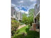 View of gray townhomes with green grass and mature trees, offering a peaceful neighborhood setting at 6836 W 84Th Cir # 15, Arvada, CO 80003