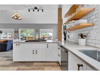 Open-concept kitchen with white cabinets, wooden shelves, and stainless steel appliances, seamlessly flowing into the living area at 32187 Sylvan Rd, Golden, CO 80403