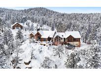 Stunning log home covered in snow, nestled amongst snow-covered trees on a hilltop, with charming architectural details at 8699 Blue Creek Rd, Evergreen, CO 80439