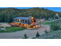 Inviting log home featuring a stone chimney, covered porch, and a wooden deck against a backdrop of lush greenery at 60 N County Highway 67, Sedalia, CO 80135