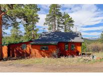 Rustic log cabin with a gray roof, surrounded by trees and with a view of snow-capped mountains in the distance at 6743 Wild Rose Ln, Evergreen, CO 80439