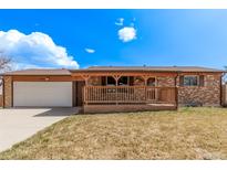 Charming brick home with a covered front porch and attached garage on a sunny day at 7720 Kendall St, Arvada, CO 80003
