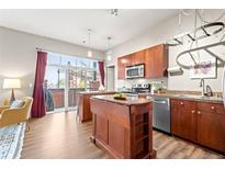 Bright kitchen features a central island, stainless steel appliances, wood cabinetry and a sliding glass door to the outside at 5401 S Park Terrace Ave # 105A, Greenwood Village, CO 80111