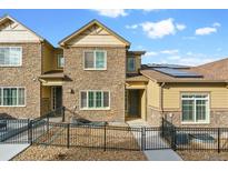 Charming townhome featuring stone accents, a fenced front yard, and solar panels on the roof at 6765 S Old Hammer Ct, Aurora, CO 80016