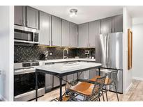 Modern kitchen features gray cabinets, stainless steel appliances, a black backsplash, and marble island with seating at 1200 Vine St # 5G, Denver, CO 80206