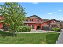 Charming red townhome with lush green lawn, mature tree, and inviting entrance at 1775 Aspen Meadows Cir, Denver, CO 80260