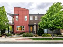 Modern townhome showcases a brick and red exterior, small yard with lush greenery at 2110 W 67Th Pl, Denver, CO 80221