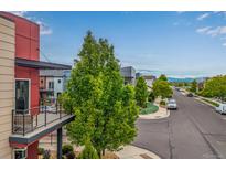 View of a modern home and street with mature trees and mountain views on a partly cloudy day at 2110 W 67Th Pl, Denver, CO 80221