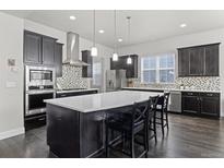 A spacious kitchen with dark cabinets, a mosaic backsplash, stainless steel appliances, and a large center island at 1867 W 137Th Ln, Broomfield, CO 80023