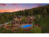 Aerial view of a luxurious home with a pool and beautiful landscaping surrounded by lush greenery at dusk at 12555 Critchell Ln, Littleton, CO 80127