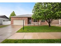 Charming brick home featuring a well-manicured lawn, mature tree, and inviting front porch at 9040 Grand Mesa Ave, Longmont, CO 80504