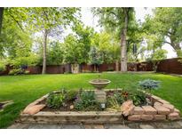 Beautiful backyard garden featuring a stone fountain, lush greenery, and a wooden privacy fence at 10000 E Ohio Ave, Denver, CO 80247