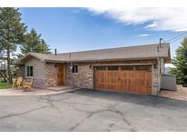 Charming single-story home featuring stone accents, a wooden garage door, and a well-maintained asphalt driveway at 24030 San Isabel Rd, Indian Hills, CO 80454