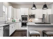 Modern kitchen with white cabinets, stainless steel appliances, granite counters, and island seating at 181 S Monaco Pkwy, Denver, CO 80224