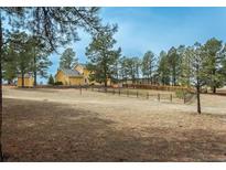 Wide shot of home's yellow exterior, surrounding trees, and large front yard enclosed by wood fence at 37677 Sable Ridge Rd, Elizabeth, CO 80107
