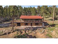 Charming home with red roof and stone accents surrounded by lush trees and a spacious deck at 34 Normandy Rd, Evergreen, CO 80439