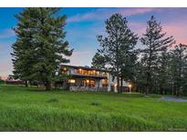 A charming two-story home featuring a large grassy yard and a deck with red chairs at 31756 Buffalo Park Rd, Evergreen, CO 80439