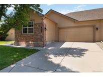 Tan home featuring a two-car garage, brick accents, and well-maintained landscaping at 16141 W 64Th Way, Arvada, CO 80007