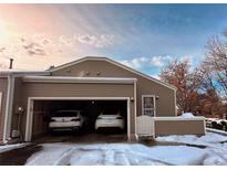 Attached garage featuring parking for two cars, with brown siding and snowy winter scenery around the home at 5898 W Asbury Pl, Lakewood, CO 80227