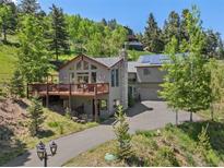 Charming multi-level home with stone chimney, large deck, and solar panels surrounded by lush trees at 32209 Blue Springs Dr, Evergreen, CO 80439