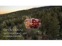 Stunning mountain home with rustic stone and wood exterior, surrounded by lush forest at dusk at 30717 Conifer Mountain Dr, Conifer, CO 80433