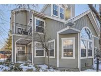 Two-story townhome with gray siding, balcony, and snowy landscaping at 6702 S Ivy Way # A1, Centennial, CO 80112