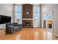 Spacious living room with a brick fireplace, hardwood floors, and natural light from large windows at 14204 E Baltic Cir, Aurora, CO 80014