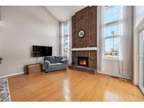 Bright living room featuring a brick fireplace, large windows with sheer curtains, and wood floors at 14204 E Baltic Cir, Aurora, CO 80014