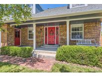 Charming brick home features a covered front porch and bright red front door with a decorative wreath at 9929 W Fairview Ave, Littleton, CO 80127