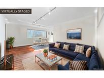 A virtually staged living room featuring a blue couch, dining table, and wood floors at 1175 N Emerson St # 308, Denver, CO 80218