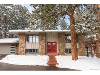 Charming stone and siding home featuring a bright red front door and snow-covered yard at 27837 Whirlaway Trl, Evergreen, CO 80439