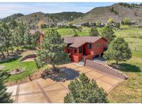 Red home exterior with a large driveway and trees, nestled in a scenic mountain setting at 10991 Expedition, Littleton, CO 80125