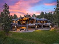 Stunning exterior view of a modern home with expansive decks and lush green lawns at sunset at 113 Elk Crossing Ln, Evergreen, CO 80439