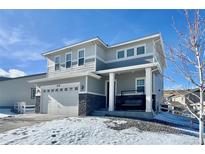 Beautiful two-story home with a porch swing, gray paint, stone accents, a two car garage and snowy front yard at 3734 Makley Cir, Castle Rock, CO 80104