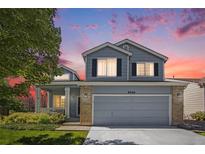 Charming two-story home featuring a covered porch, manicured lawn, and brick accents at dusk at 9200 W Indore Dr, Littleton, CO 80128