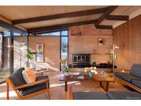 Mid-century living room featuring wood paneling, exposed beams, a brick fireplace, and stylish, vintage furniture at 5450 Mohawk Rd, Littleton, CO 80123