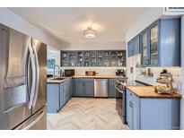 Modern kitchen with blue cabinetry, stainless steel appliances, butcher block countertops, and herringbone-patterned floors at 1655 S Lowell Blvd, Denver, CO 80219